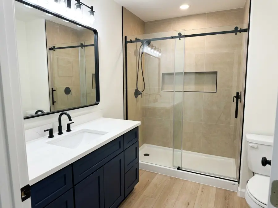 Custom tiled walk-in shower with black-framed sliding glass replacing the old insert